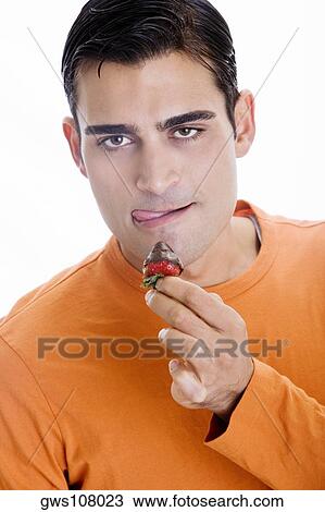 Stock Image - Portrait of a mid adult man holding a chocolate dipped strawberry in front of his mouth. Fotosearch