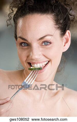 Stock Image - Portrait of a young woman eating a cucumber slice. Fotosearch