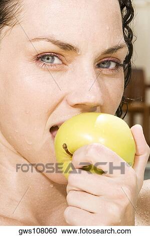 Stock Image - Portrait of a young woman eating a green apple in a swimming pool. Fotosearch