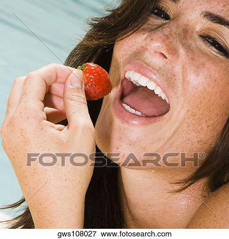 Stock Photo - Portrait of a young woman eating a strawberry. Fotosearch