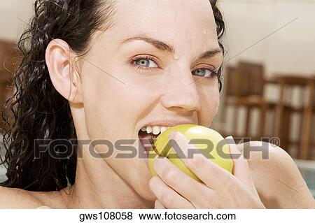 Stock Photo - Portrait of a young woman eating a green apple. Fotosearch