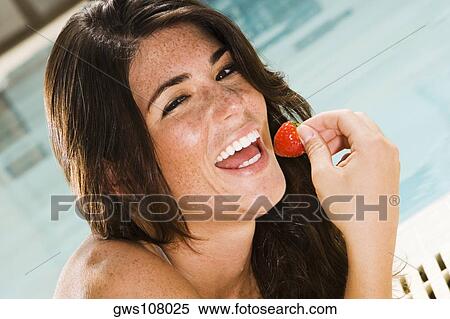 Stock Photography - Portrait of a young woman eating a strawberry at the poolside. Fotosearch