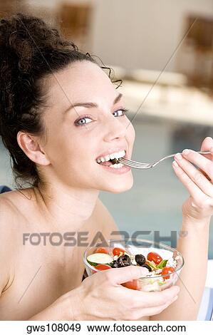 Portrait of a young woman eating salad with a fork at the poolside View Large Photo Image Stock Photo - Portrait of a young woman eating salad with a fork at the poolside. Fotosearch
