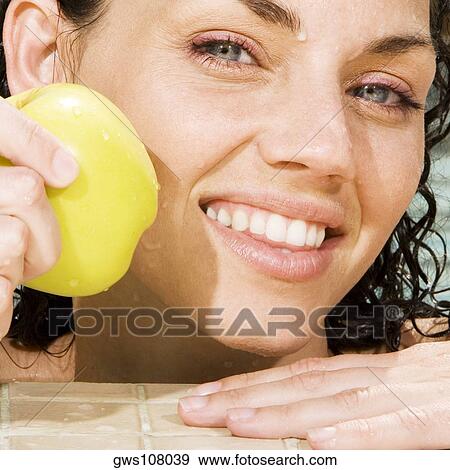 Stock Photo - Portrait of a young woman holding a green apple in a swimming pool. Fotosearch