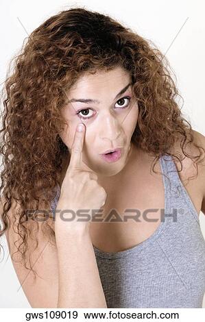 Stock Photo - Portrait of a young woman pointing at her eye. Fotosearch