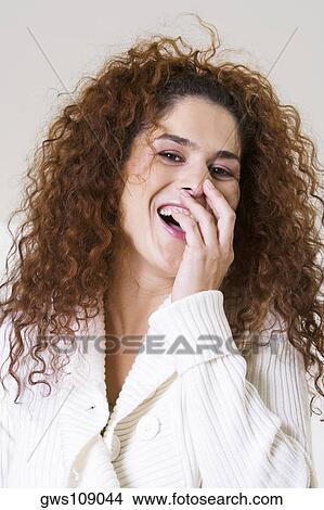 Picture - Portrait of a young woman smiling with her hand on her mouth. Fotosearch