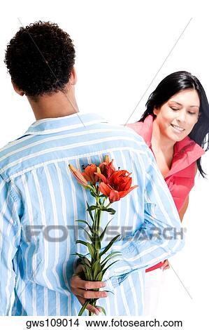 Rear view of a young man standing in front of a young woman with flowers behind his back View Large Photo Image Picture - Rear view of a young man standing in front of a young woman with flowers behind his back. Fotosearch