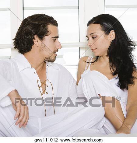 Close-up of a young couple sitting on the bed and looking at each other View Large Photo Image Stock Image - Close-up of a young couple sitting on the bed and looking at each other. Fotosearch