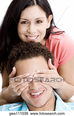 Stock Photo - Portrait of a young woman covering the eyes of a young man. Fotosearch