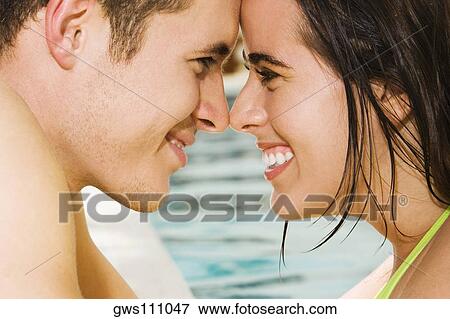 Stock Photo - Side profile of a young couple looking at each other at the poolside. Fotosearch