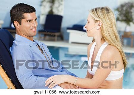 Stock Photograph - Young woman and a mid adult man sitting at the poolside. Fotosearch