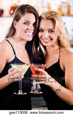 Portrait of two young women toasting martinis in a bar View Large Photo Image Stock Photograph - Portrait of two young women toasting martinis in a bar. Fotosearch