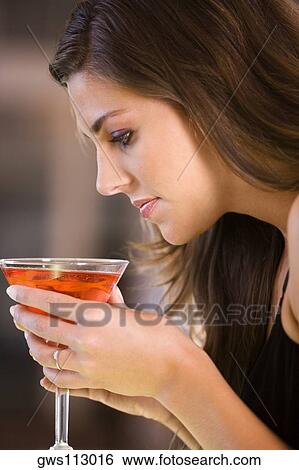 Stock Photograph - Side profile of a young woman holding a glass of martini. Fotosearch
