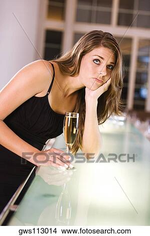 Picture - Young woman leaning over a bar counter holding a champagne flute. Fotosearch