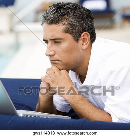 Stock Image - Close-up of a mid adult man lying down in front of a laptop. Fotosearch