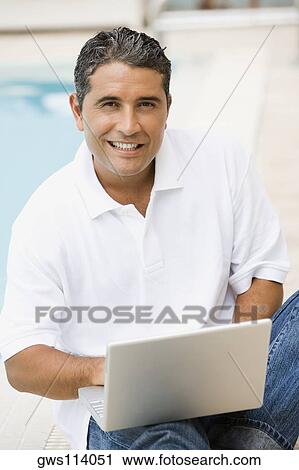 Portrait of a mid adult man using a laptop at the poolside View Large Photo Image Stock Image - Portrait of a mid adult man using a laptop at the poolside. Fotosearch