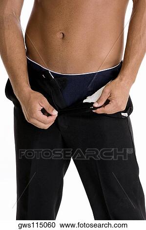 Stock Image - Mid section view of a man taking off his pants. Fotosearch