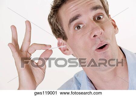 Stock Image - Portrait of a young man using a cotton swab in his ear. Fotosearch