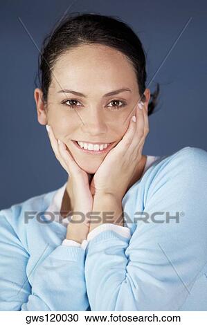 Stock Image - Portrait of a young woman with her hands on her face smiling. Fotosearch