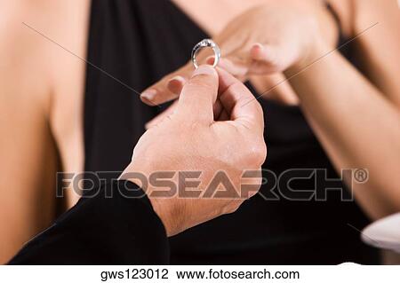 Close-up of a man putting an engagement ring on a young woman's finger View Large Photo Image Stock Image - Close-up of a man putting an engagement ring on a young woman's finger. Fotosearch