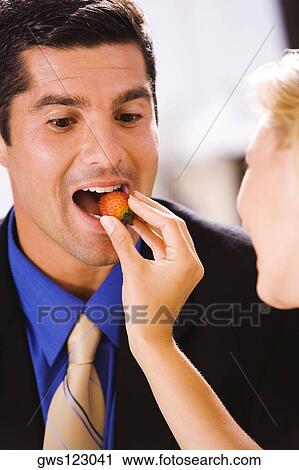 Stock Image - Close-up of a young woman feeding a mid adult man a strawberry. Fotosearch