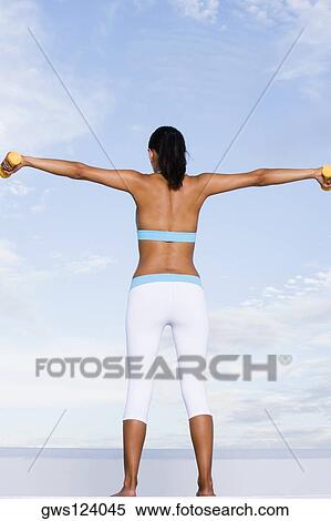 Stock Photography - Low angle view of a young woman exercising with dumbbells. Fotosearch