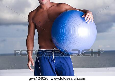 Mid section view of a man holding a fitness ball View Large Photo Image Stock Photograph - Mid section view of a man holding a fitness ball. Fotosearch