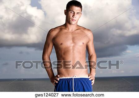 Portrait of a young man standing bare chested on the beach View Large Photo Image Stock Photo - Portrait of a young man standing bare chested on the beach. Fotosearch