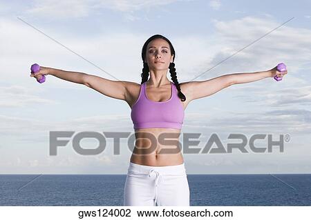 Stock Image - Portrait of a young woman exercising with dumbbells. Fotosearch