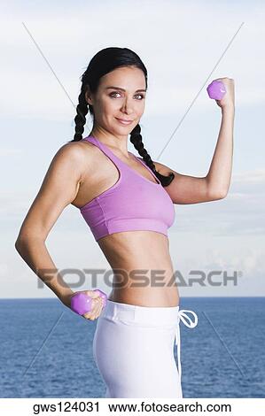 Stock Image - Portrait of a young woman exercising with dumbbells. Fotosearch