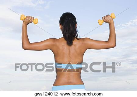 Rear view of a young woman lifting dumbbells View Large Photo Image Stock Image - Rear view of a young woman lifting dumbbells. Fotosearch