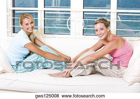 Stock Photo - Portrait of two young women sitting on a bed. Fotosearch