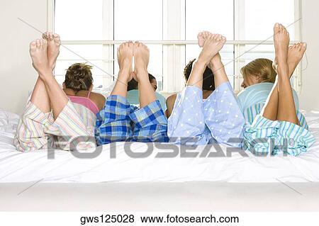Rear view of four young women lying down side by side on a bed View Large Photo Image Stock Photo - Rear view of four young women lying down side by side on a bed. Fotosearch