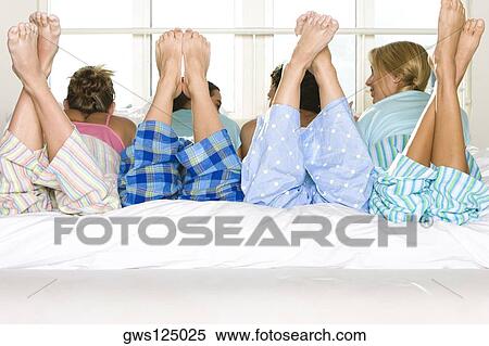 Stock Photography - Rear view of four young women lying down side by side on a bed. Fotosearch