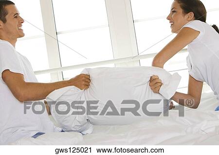 Stock Image - Side profile of a young couple having a pillow fight. Fotosearch