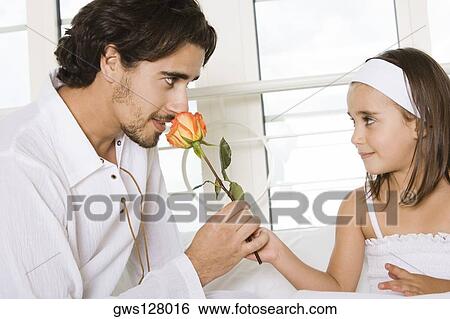 Stock Photograph - Close-up of a father sitting with his daughter smelling a rose. Fotosearch