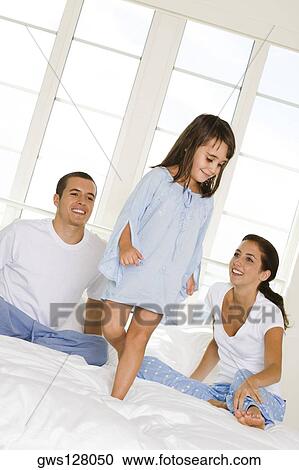 Girl standing on the bed in front of her parents View Large Photo Image Stock Image - Girl standing on the bed in front of her parents. Fotosearch