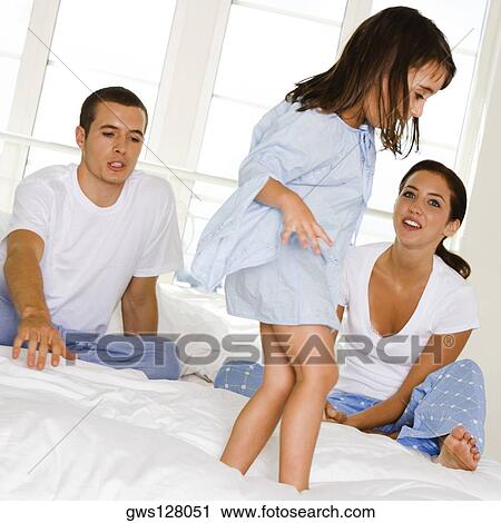 Stock Image - Girl standing on the bed in front of her parents. Fotosearch