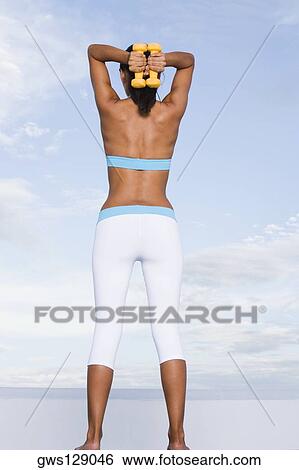 Low angle view of a young woman exercising with dumbbells View Large Photo Image Stock Photograph - Low angle view of a young woman exercising with dumbbells. Fotosearch