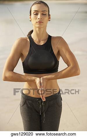 Stock Image - Mid adult woman standing in the prayer position with her eyes closed. Fotosearch