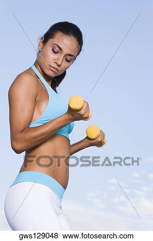 Side profile of a young woman exercising with dumbbells View Large Photo Image Stock Photo - Side profile of a young woman exercising with dumbbells. Fotosearch