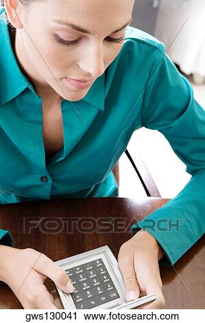 Stock Image - High angle view of a young woman using a calculator. Fotosearch