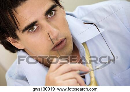 Stock Photo - Portrait of a businessman holding a pair of eyeglasses. Fotosearch