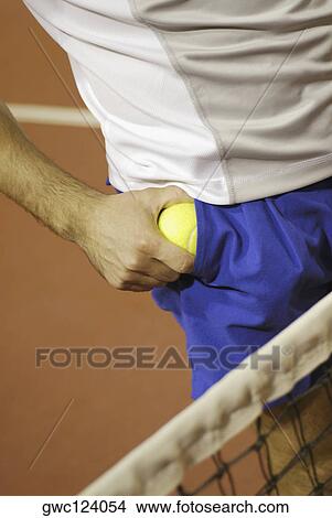 Picture - Mid section view of a man taking out a tennis ball from his pocket. Fotosearch