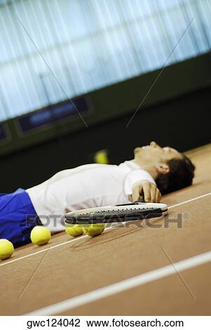 Stock Image - Side profile of mid adult man lying on a tennis court. Fotosearch