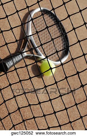 Stock Image - High angle view of a tennis racket and a tennis ball behind a tennis net. Fotosearch