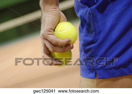 Stock Image - Mid section view of a man holding two tennis balls. Fotosearch