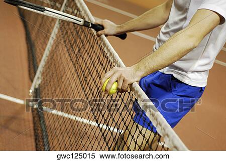 Stock Photography - Mid section view of a man leaning against a tennis net. Fotosearch