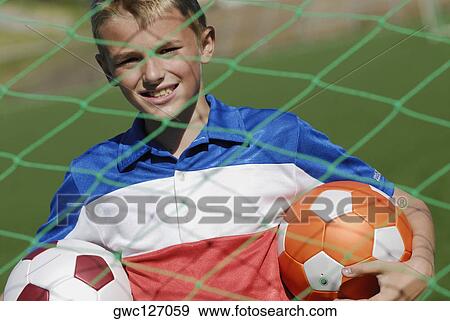 Portrait of a soccer player standing behind the net and holding two soccer balls View Large Photo Image Stock Photo - Portrait of a soccer player standing behind the net and holding two soccer balls. Fotosearch