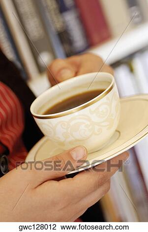 Stock Image - Close-up of a human hand holding a cup of black tea. Fotosearch